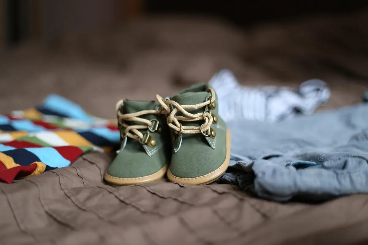 Pair of small green baby shoes on a bed beside folded clothes