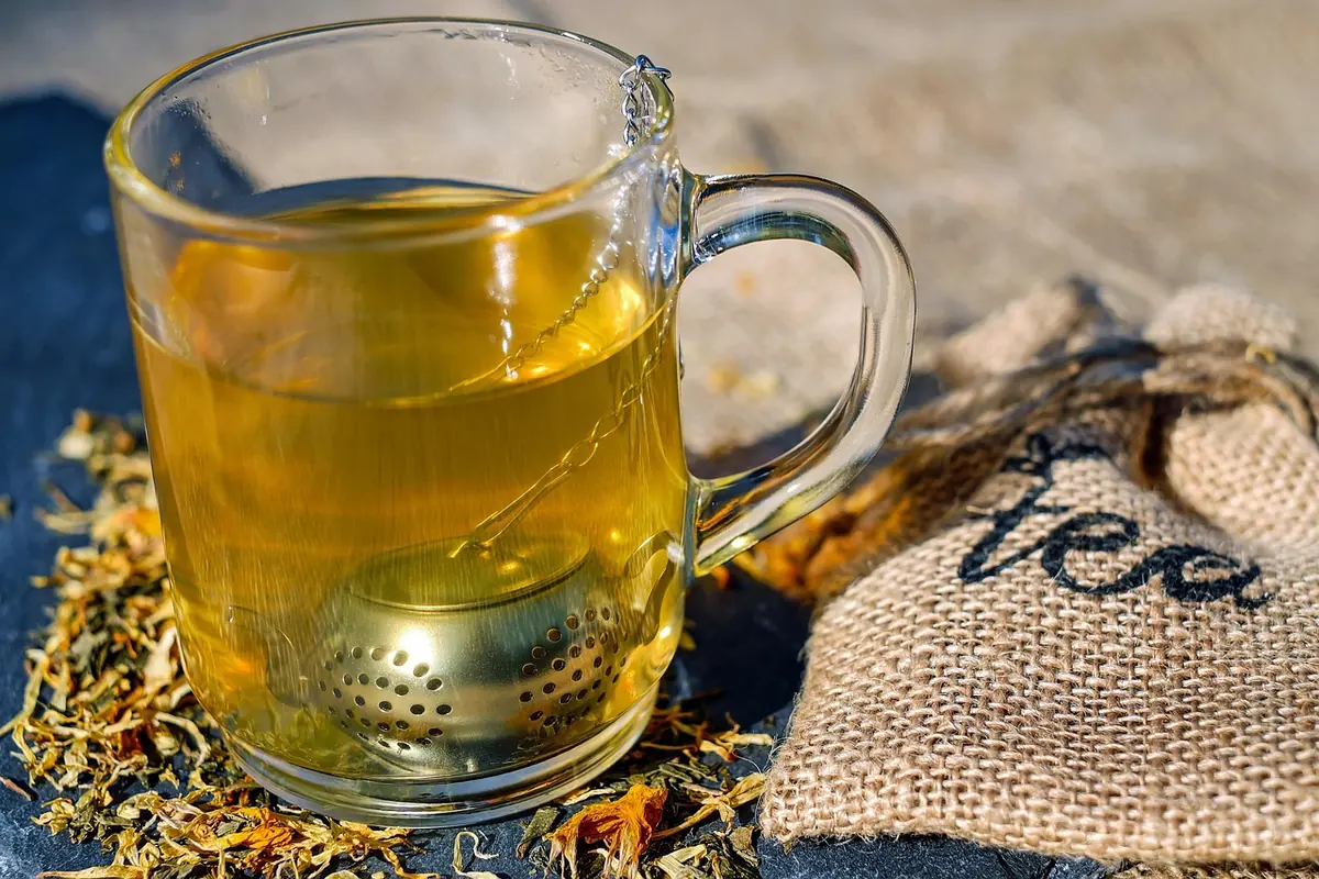 Glass mug of tea with a tea infuser beside a burlap tea bag